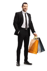 Man in a black suit holding shopping bags and smiling
