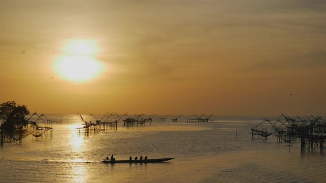 Long boats are floating across the lake and fishnet lifting under beautiful sunrise time located at Khlong Pak Pra, Phatthalung province of Thailand