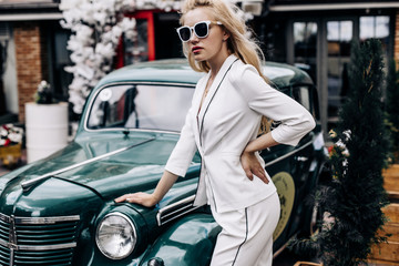 Fashion photo. A model wearing sunglasses poses near a green retro car.