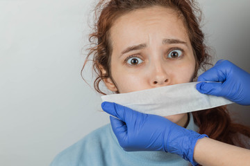 A Caucasian woman with sticky tape gluing her mouth. Hands in gloves hold a vow. The victim of...