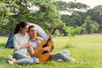 Picnic and Camping time. Young couple having fun with guitar on picnic and Camping in the park. Love and tenderness, Romantic man playing guitar to his girlfriend, lifestyle and valentine concept