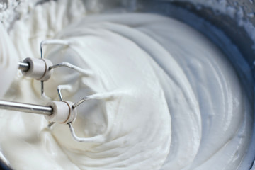  Beating a white cream with a mixer in a metal bowl. Whipped cream. Cream for the cake.
