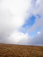 Fototapeta na wymiar Wide vertical view of stratocumulus clouds parting the grassy moors of Dartmoor on a sunny day. Devon, United Kingdom. Travel and nature.