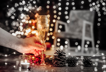 Spending Christmas holidays alone and drinking champagne alone, Holiday depression and alcoholism concept. Selective focus on hand with alcohol glass goblet and blurred party lights on background.