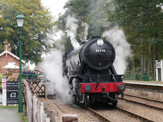 old steam locomotive train with steam billowing around and onto tracks