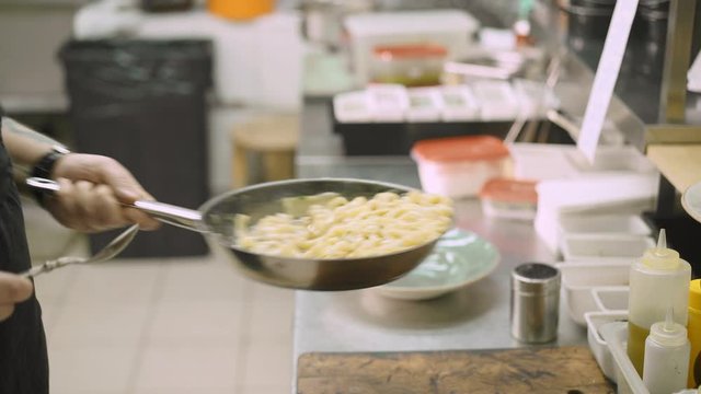Close up handheld shot of chef male hand cooking tossing pappardelle in the frying pan in italian restaurant. Close up of male hand and pan with spaghetti