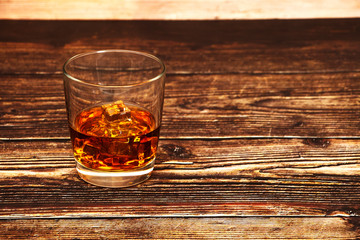 Whiskey with ice or brandy in a glass and a square carafe on an old wooden background. Whiskey with ice in a glass. Whiskey or cognac. Selective focus.