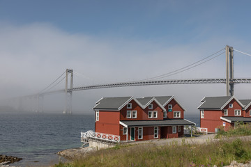 A misty bridge and classic red rorbuer homes in Lofoten, Norway