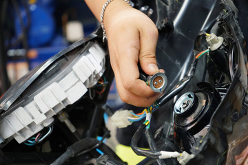 Fototapeta na wymiar Motorcycle mechanic repair and change scooter headlamp bulb at motorcycle garage