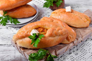 Rasstegai pie of yeast dough with meat filling on white wooden table. Traditional meal of Russian cuisine