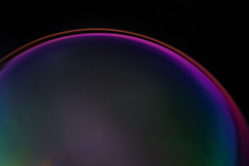 Close-up and detailed view of an iridescent, colorful soap bubble glowing in the light against a dark background in rainbow colors