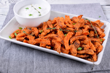 Spicy sweet potato fried sticks and yogurt sauce served on white ceramic plate