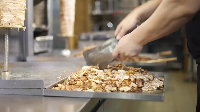 Close up handheld shot of chef cutting meat for shawarma on a metal plate under a skewer. Male hands cutting beef with two knives for shawarma