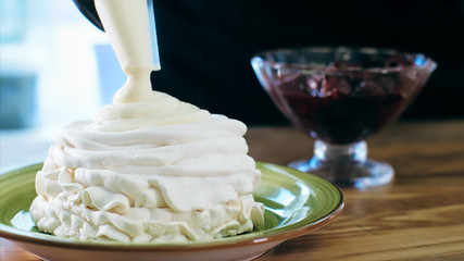 Chef cooking meringue cake with cream, close-up. Cook using pastry bag for filling meringue while preparing sweet dessert.
