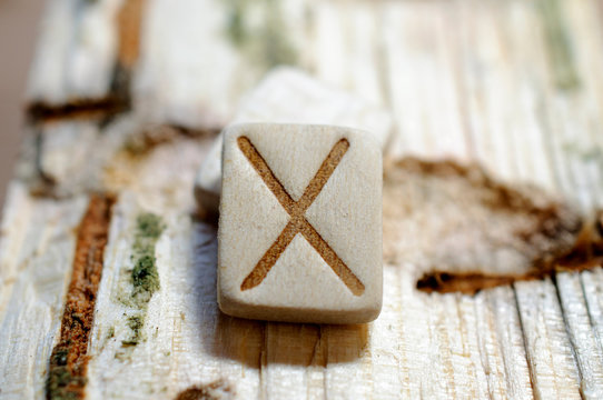 Wooden rune Gebo close-up on a wooden background. Soft focus