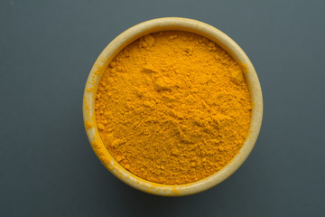 Defocused top view at turmeric powder in ceramic bowl at pastel gray color background. Alternative medicine.