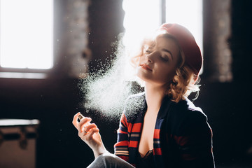 A beautiful blonde woman in a red beret holds a small bottle in her hands spraying perfume on...