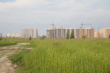 Road through green grass to construction site with houses in a new residential complex