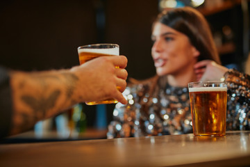 Close up of couple sitting next to bar counter, drinking beer and flirting.