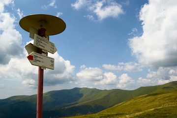 Directional sign post in the mountains with peak names and arrows with translation on English...
