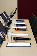 Conference room table for business meeting with microphones, monitors, pens, papers, glasses for water and chairs in row, selective focus