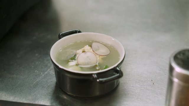 Close up handheld shot of chef decorating ukha fish soup with a slices radish and green olive oil. Ukha fish soup cooked in the restaurant ready to serve