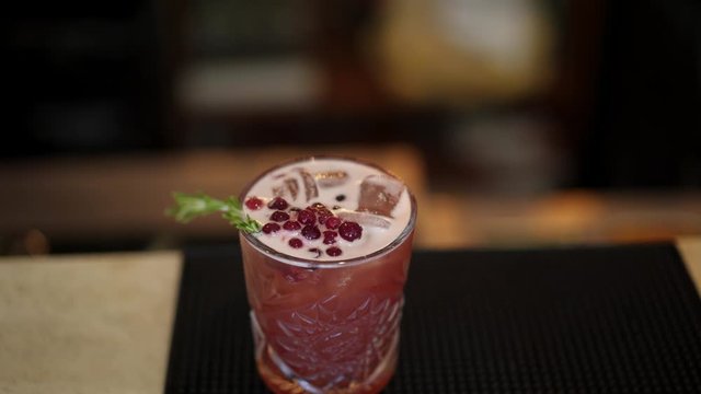 Close up pan macro shot of red cocktail with cubes of ice, decorated with red currants and pine. Pan shot macro top view of red cocktail with berries and pine branch