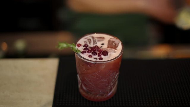 Close up macro shot of red cocktail with cubes of ice, decorated with red currants and pine. Pan shot macro top view of red cocktail with berries and pine branch