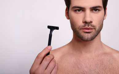 A beauty man with a slight unshaven face holds a black razor