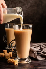 male hand pouring milk into hot black tea front view on dark background