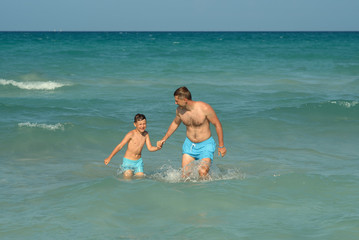 Fototapeta premium Dad and son coming out of water at sea shore.