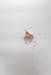 broken cigarette in a triangle shape with tobacco crumbles on white gradient background 