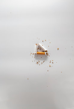 broken cigarette in a triangle shape with tobacco crumbles on white gradient background 