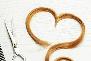Heart made of cut hair curl and scissors. White wooden background