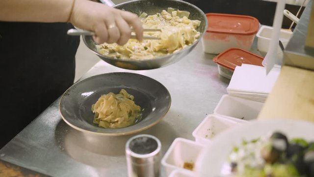 Close up handheld shot of chef male laying out pappardelle in the plate from the frying pan in the kitchen of italian restaurant. Close up of chef male serving pappardelle