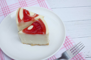 two pieces of cheesecake on a plate and a fork on tablecloths on white wooden background flat lay