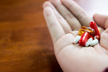 Close up of colorful pills and medicines in the hand over blurred wooden background with copy space. Selective focus with shallow depth of field.