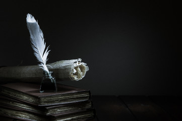 Quill pen and rolled papyrus sheets on a wooden table with old books, high contrast - 311625210