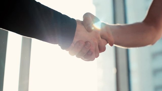 Close-up of two business men handshake on the sunrise background. Tracking shot in slow motion.