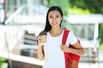 Beautiful young woman with paper cup and backpack on the street