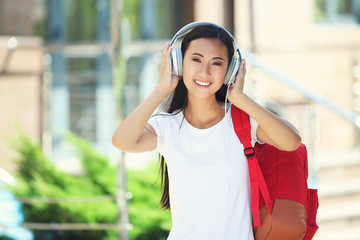 Beautiful young woman with headphones and backpack on the street