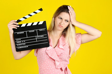 Young woman with blank clapper board on yellow background