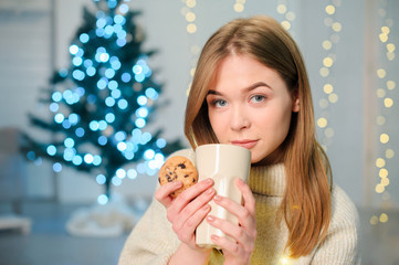 girl in sweater with a cup of hot drink on the background of Christmas decor, Christmas home comfort