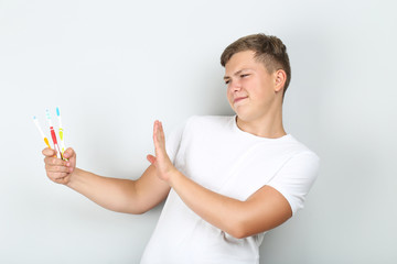 Young man with toothbrushes showing stop gesture on grey background