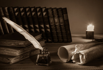 Quill pen and rolled papyrus sheets with old books at candle light, sepia effect
