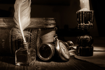 Quill pen and rolled papyrus sheets with old books at candle light, sepia effect