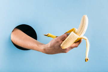 A woman's hand pulls a peeled banana out of a black hole in a blue paper wall.