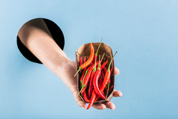 A woman's hand pulls a box of chili peppers out of a black hole in a blue paper wall.