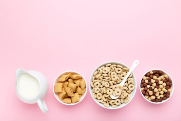 Various corn flakes with milk in jar and spoon on pink background