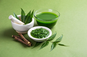 Medicinal Neem leaves in mortar and pestle with neem paste, juice and twigs on green background